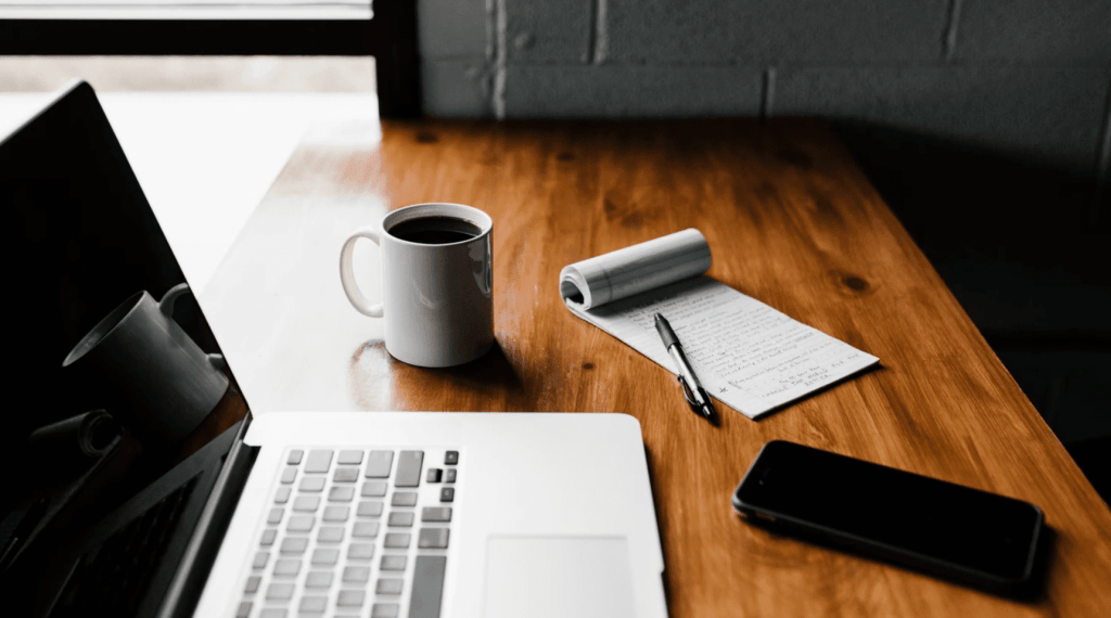 laptop, coffee mug, phone, and notepad on desk - a freelance content marketer working on a content marketing strategy for a company